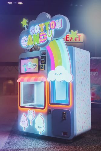 An illuminated The Merch Avenue cotton candy kiosk in a venue at night